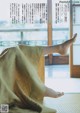 A woman's bare feet sitting on a bed in front of a window.