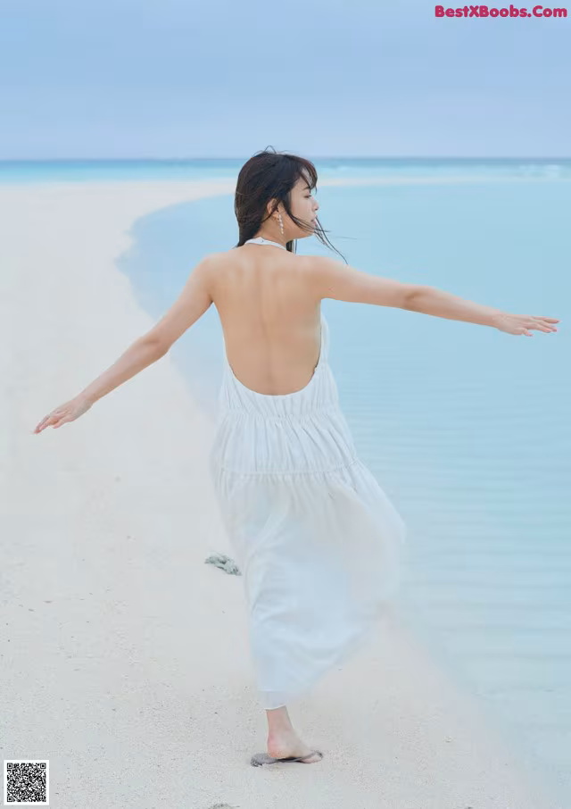A woman in a white dress standing on a beach.