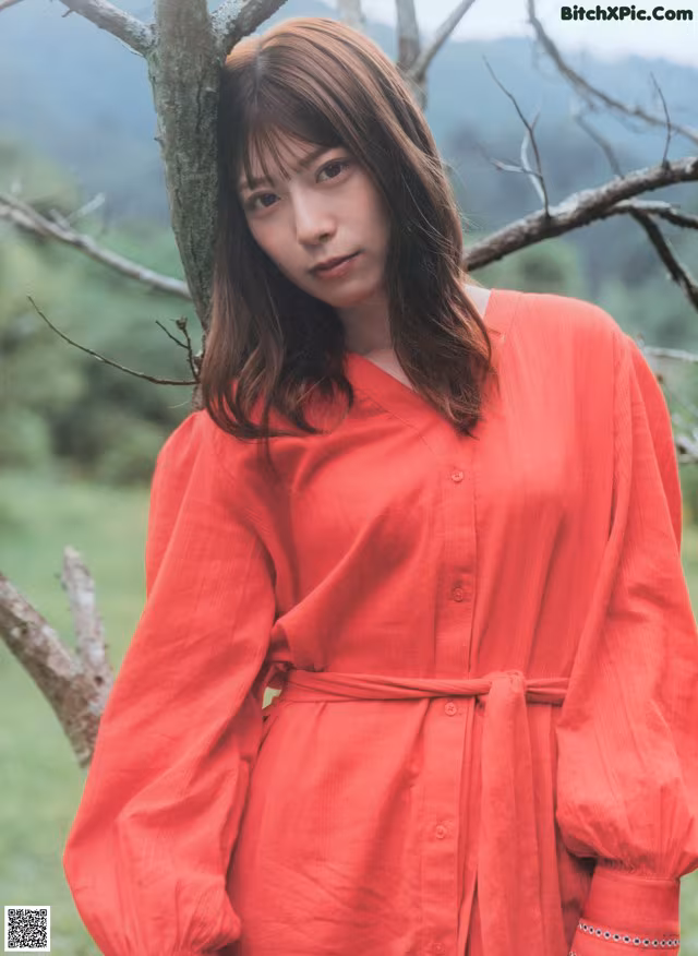 A woman in a red dress standing next to a tree.