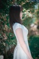 A woman in a white dress standing in front of a tree.