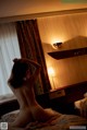 A naked woman sitting on a bed in a hotel room.