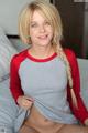 A woman in a red and gray shirt is sitting on a bed.