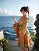 A woman in a yellow kimono standing by the ocean.