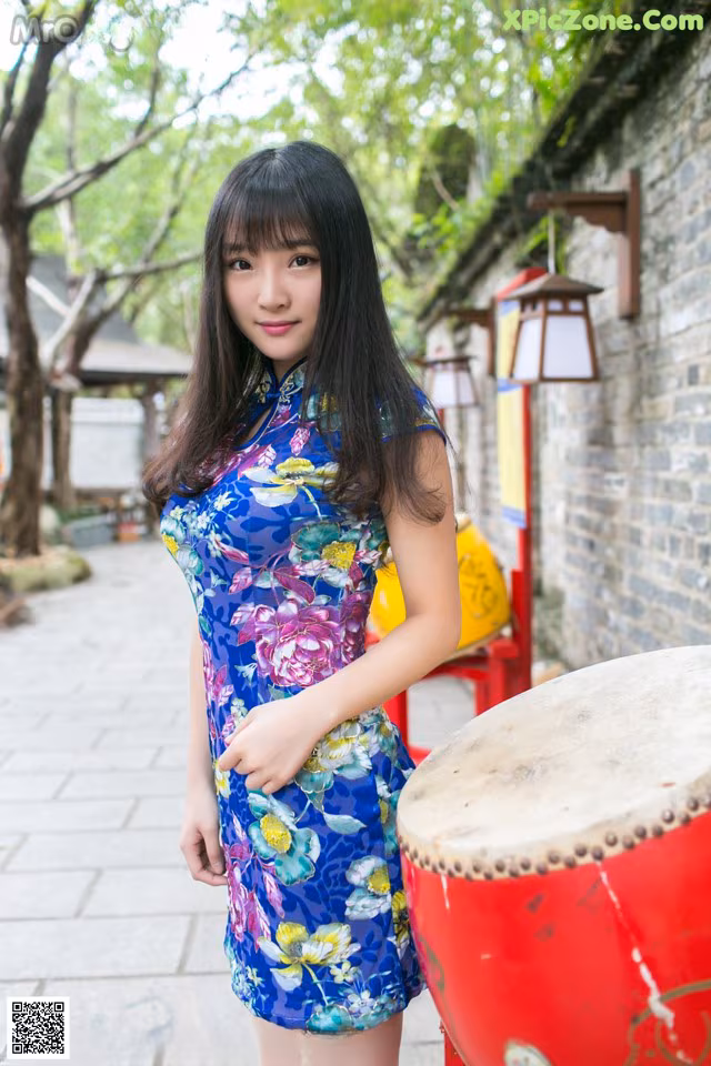 A woman in a blue dress standing next to a red drum.