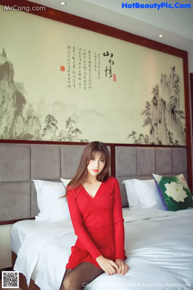 A woman in a red dress sitting on a bed.