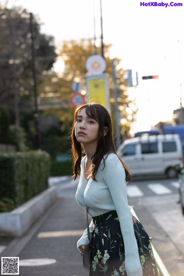 A woman standing on the side of a street next to a traffic light.